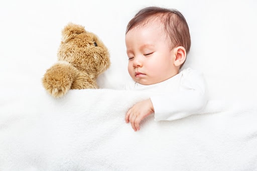 A toddler sleeps peacefully with teddy bear on his side