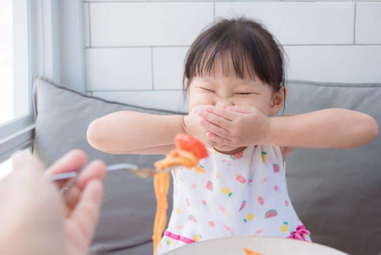 A little girl refuses to eat when her mom tries to feed her food